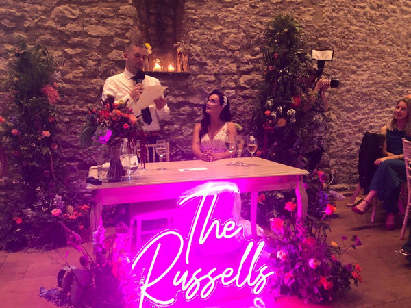 'The Russells' neon name sign glowing pink at a wedding top table