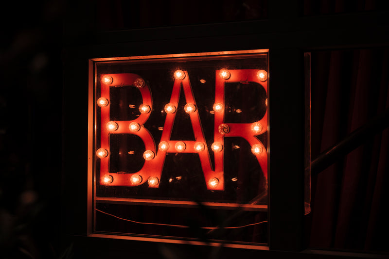 Outdoor bar sign glowing in neon lights on a dark street at night