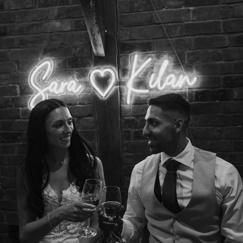 A black and white image of a bride and groom in front of a white LED neon sign from neon day at a wedding ceremony